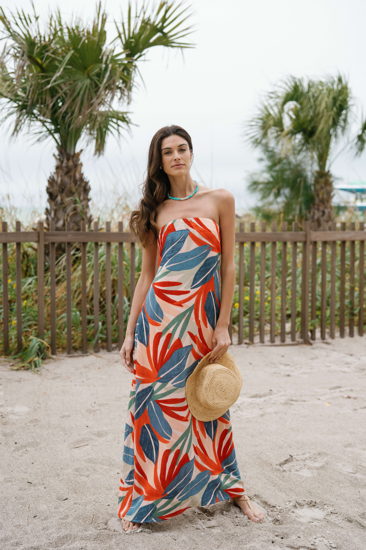 Strapless palm print maxi dress standing pose, orange and blue leaf pattern