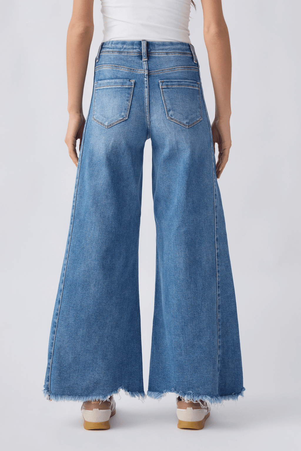 Back view of medium wash high-rise ultra wide leg jeans with yoke seams and frayed hem.