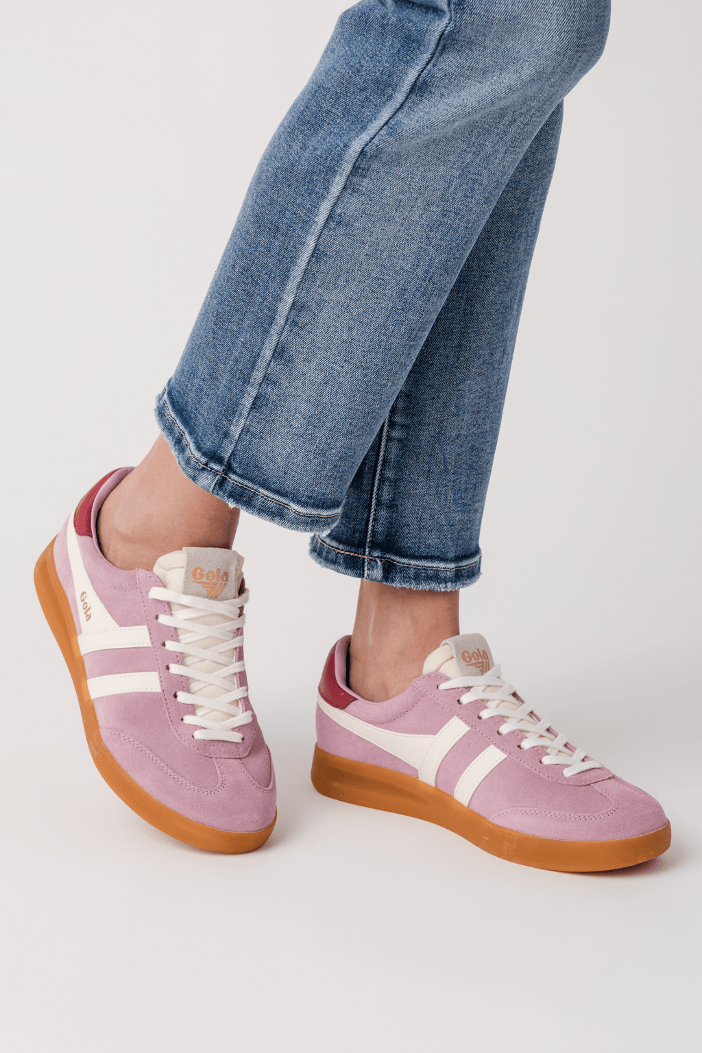 Pink sneakers with white stripes and gum outsole, angled side view