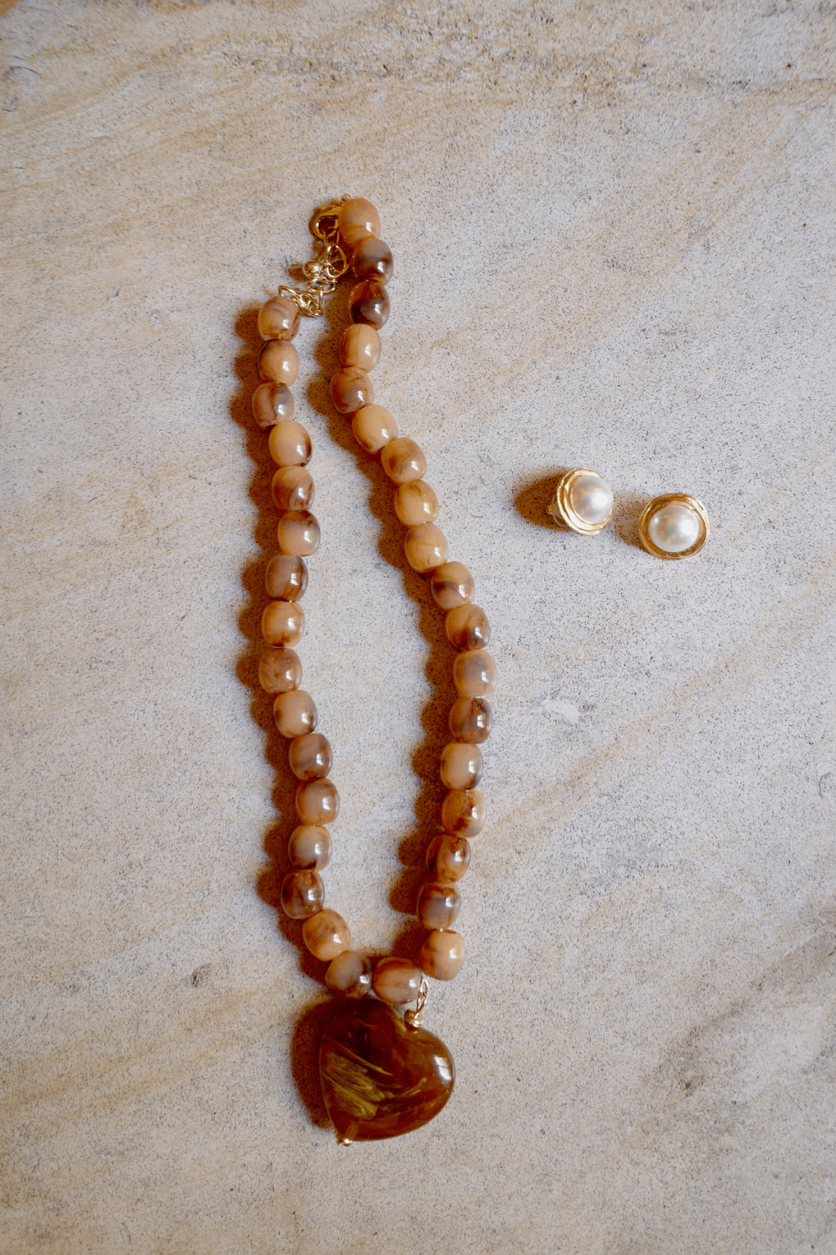 Pair of gold-tone hoop earrings with round pearl on stone surface