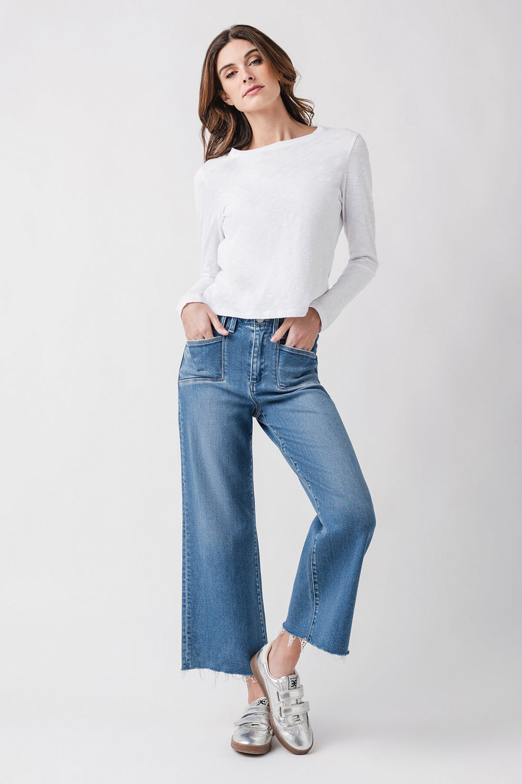 Medium wash ankle flare jeans on model with frayed cuffs and button fly