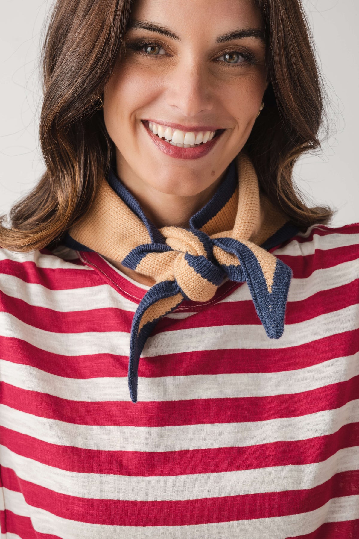 Khaki triangle knit scarf with striped ends, tied in a loose knot at the neck