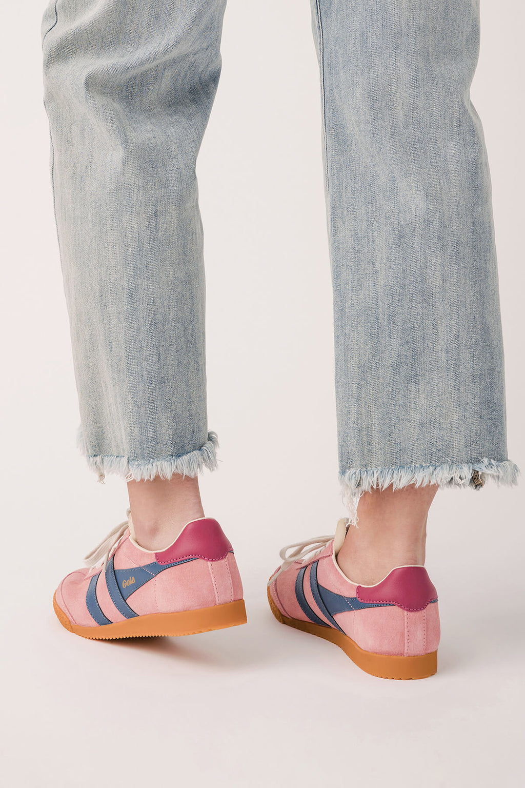Pink low-top sneakers with striped sides and gum sole, worn with frayed light jeans.