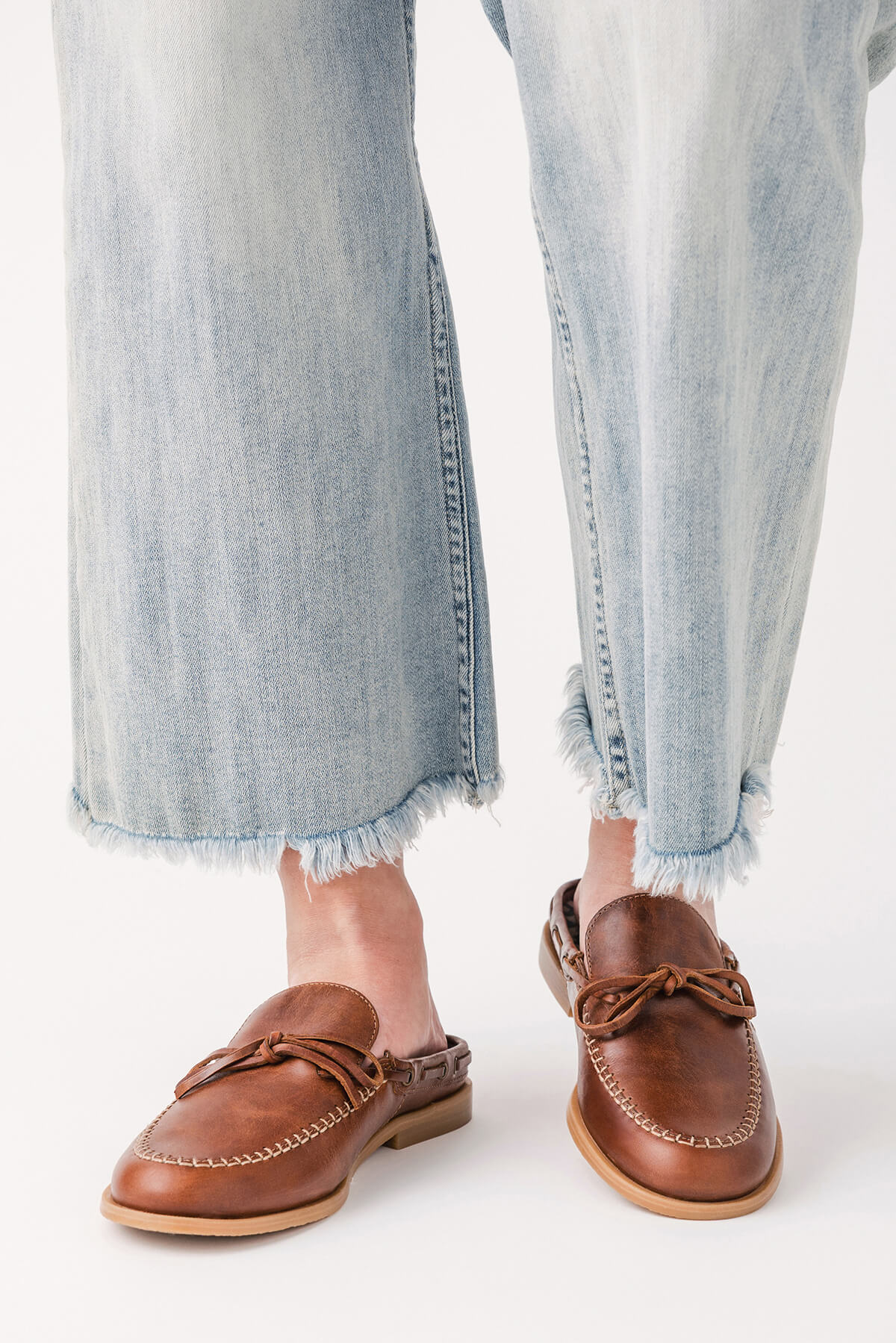 Brown mule loafer shoes with stitched detailing, braided tassel ties, and flat sole