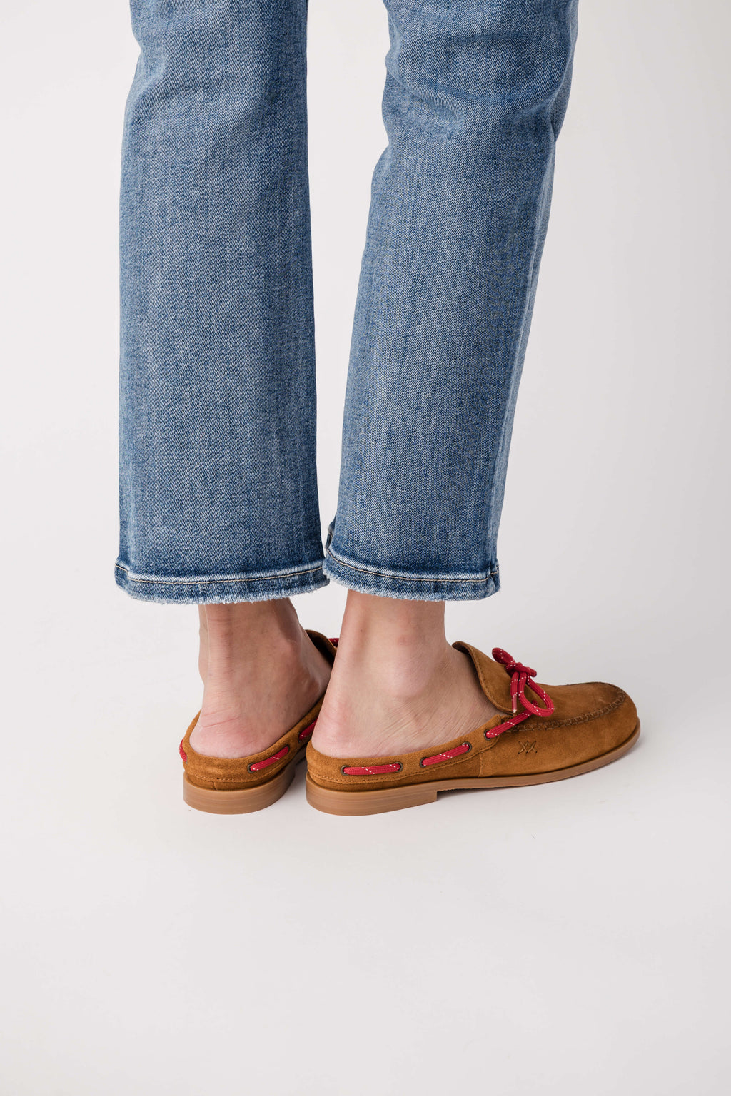 Brown suede mule flats with red tie bow, worn with cuffed blue jeans
