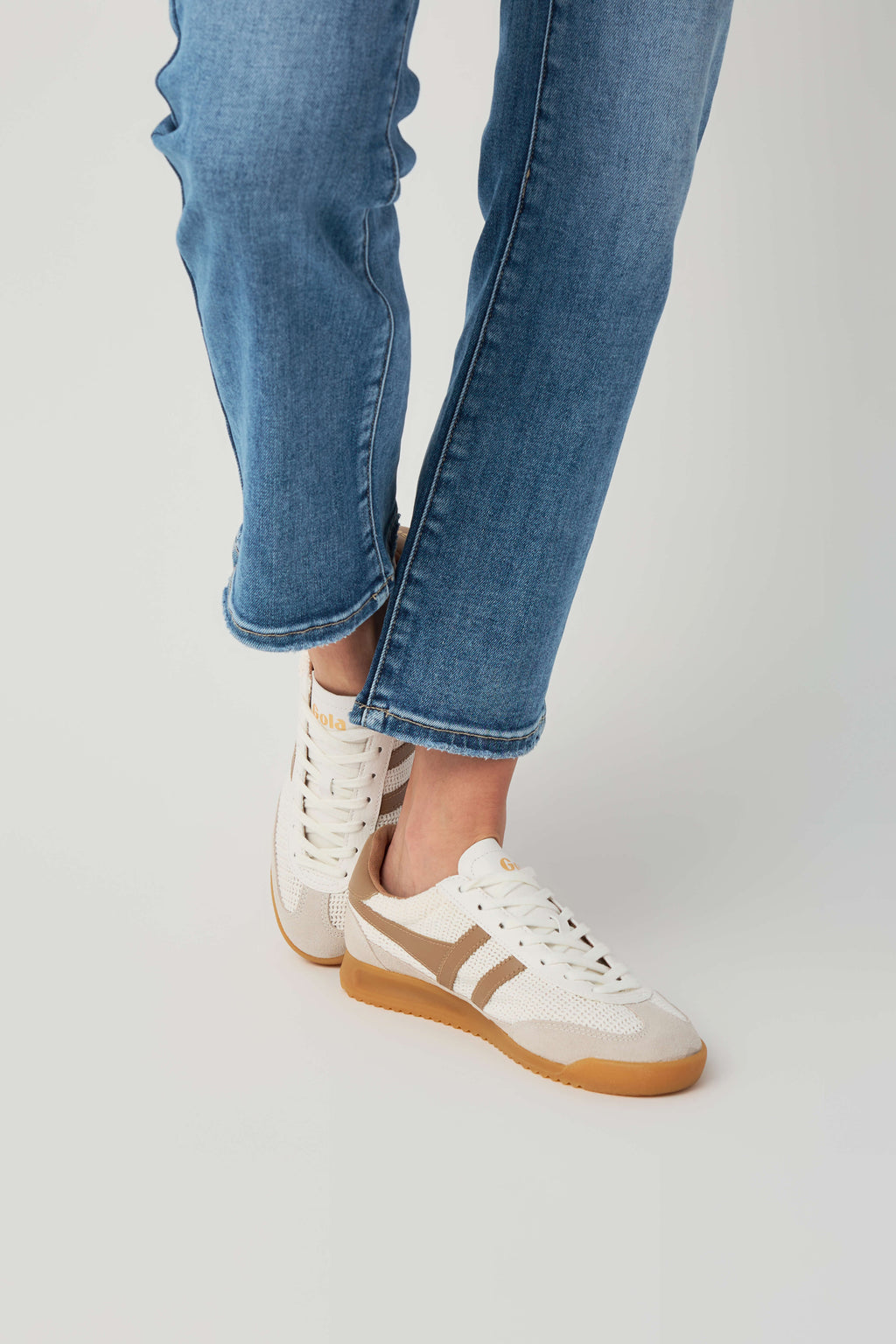 Off-white and tan low-top sneakers on feet, lace-up style with gum outsole