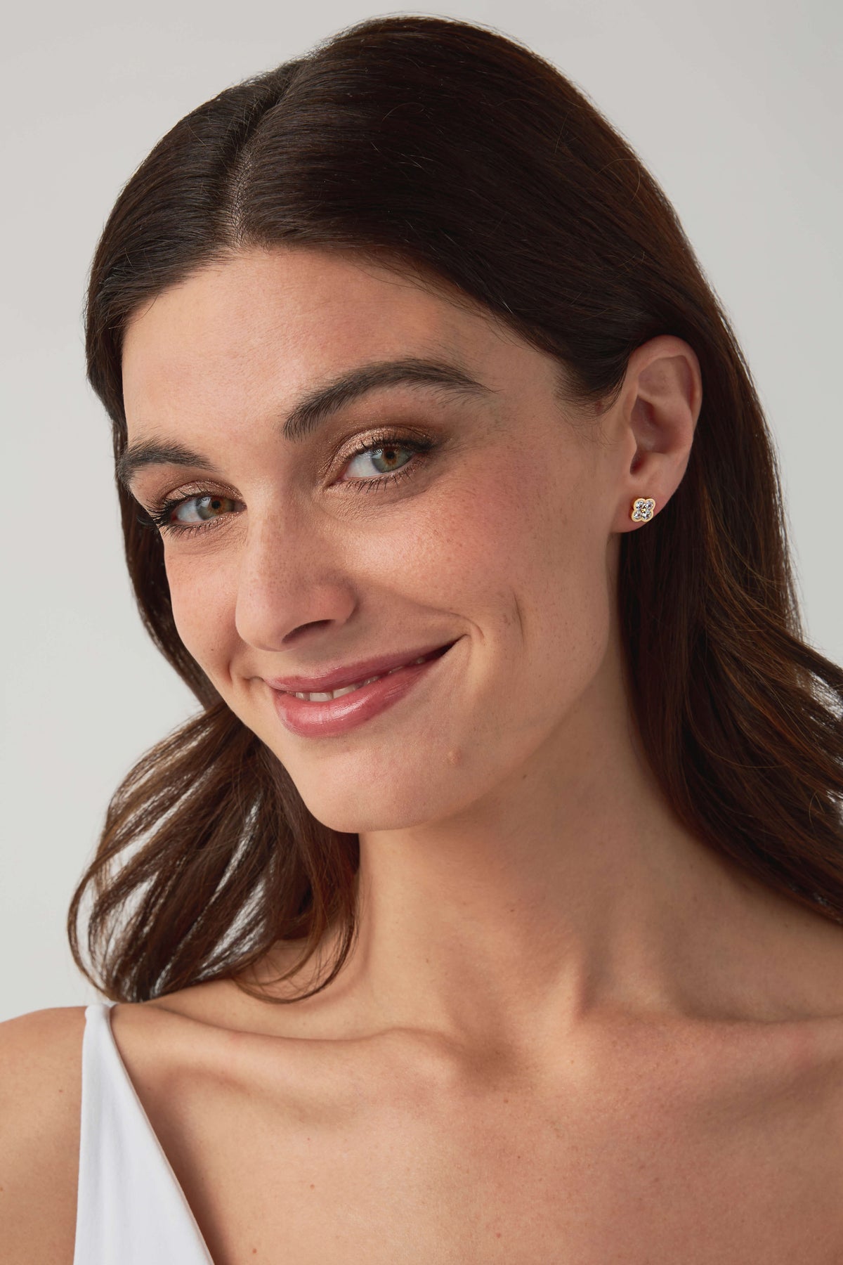Gold floral stud earrings with round clear stones, shown on model's ear