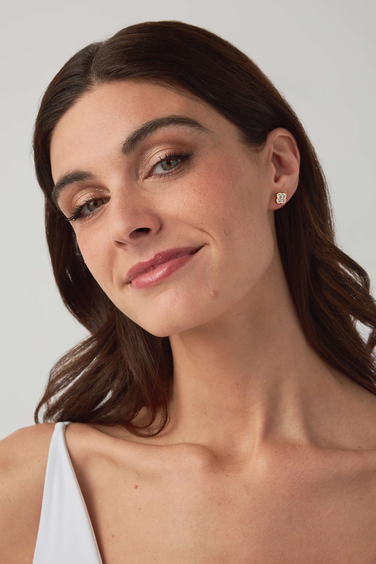 Gold floral stud earrings with round clear stones, close-up on ear