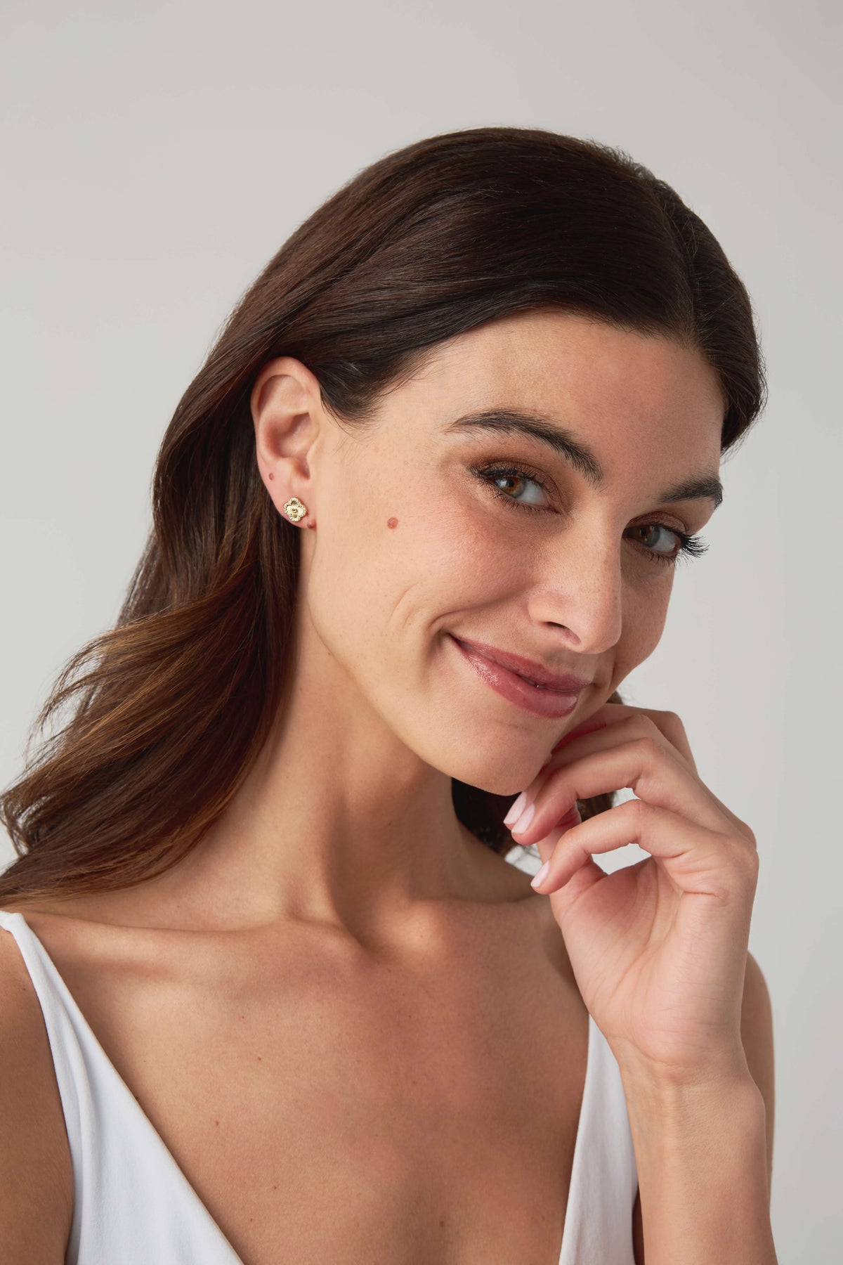 Gold stud earrings with small circular icon design visible on the ear