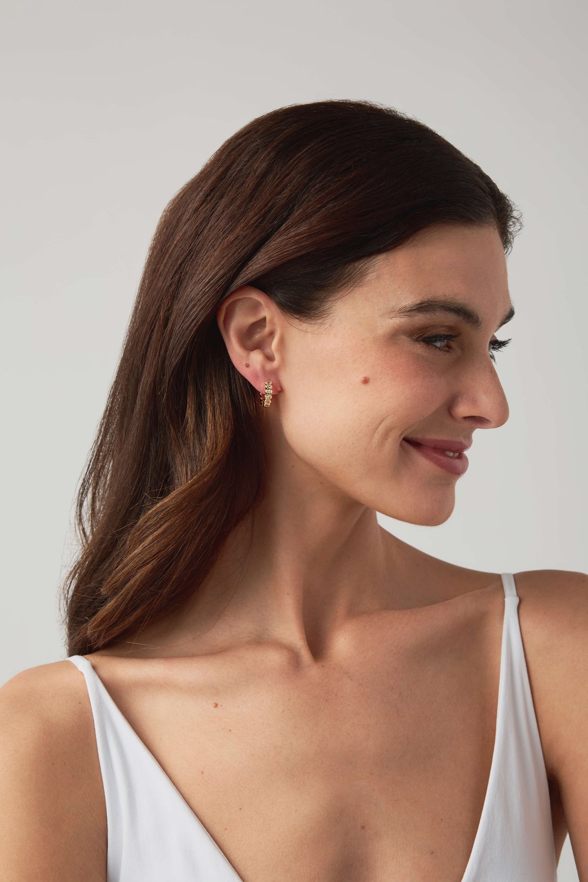 Gold hoop earrings with a row of sparkling round stones on a model