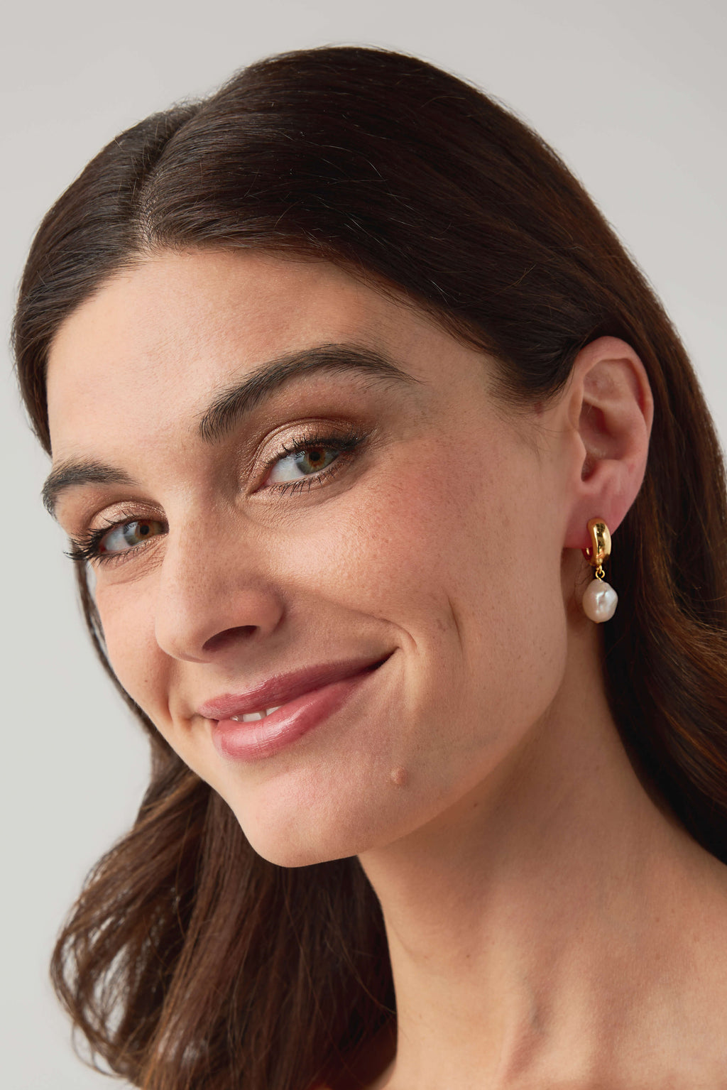 Gold hoop earrings with white pearl drop, worn close-up