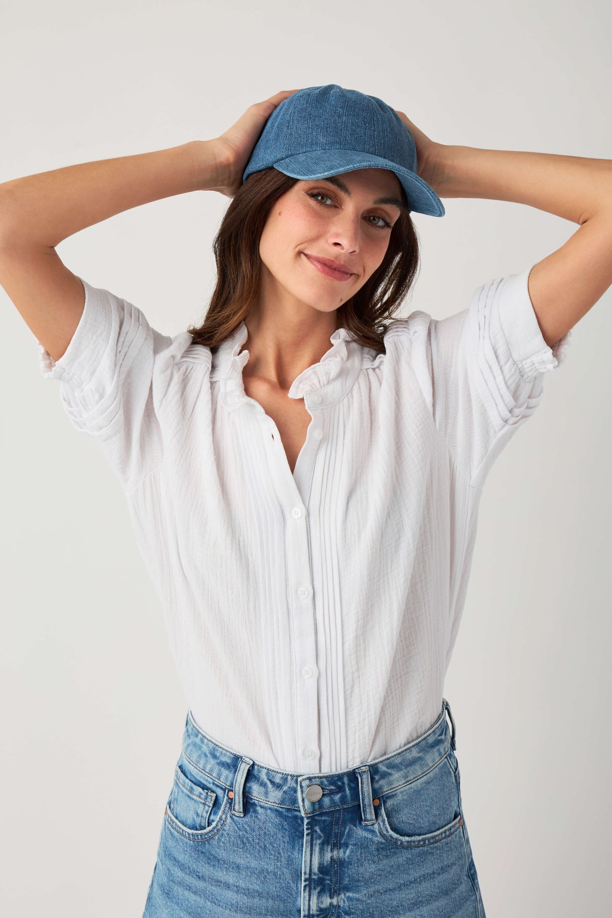 Denim blue baseball cap with curved brim, styled on model with hands overhead