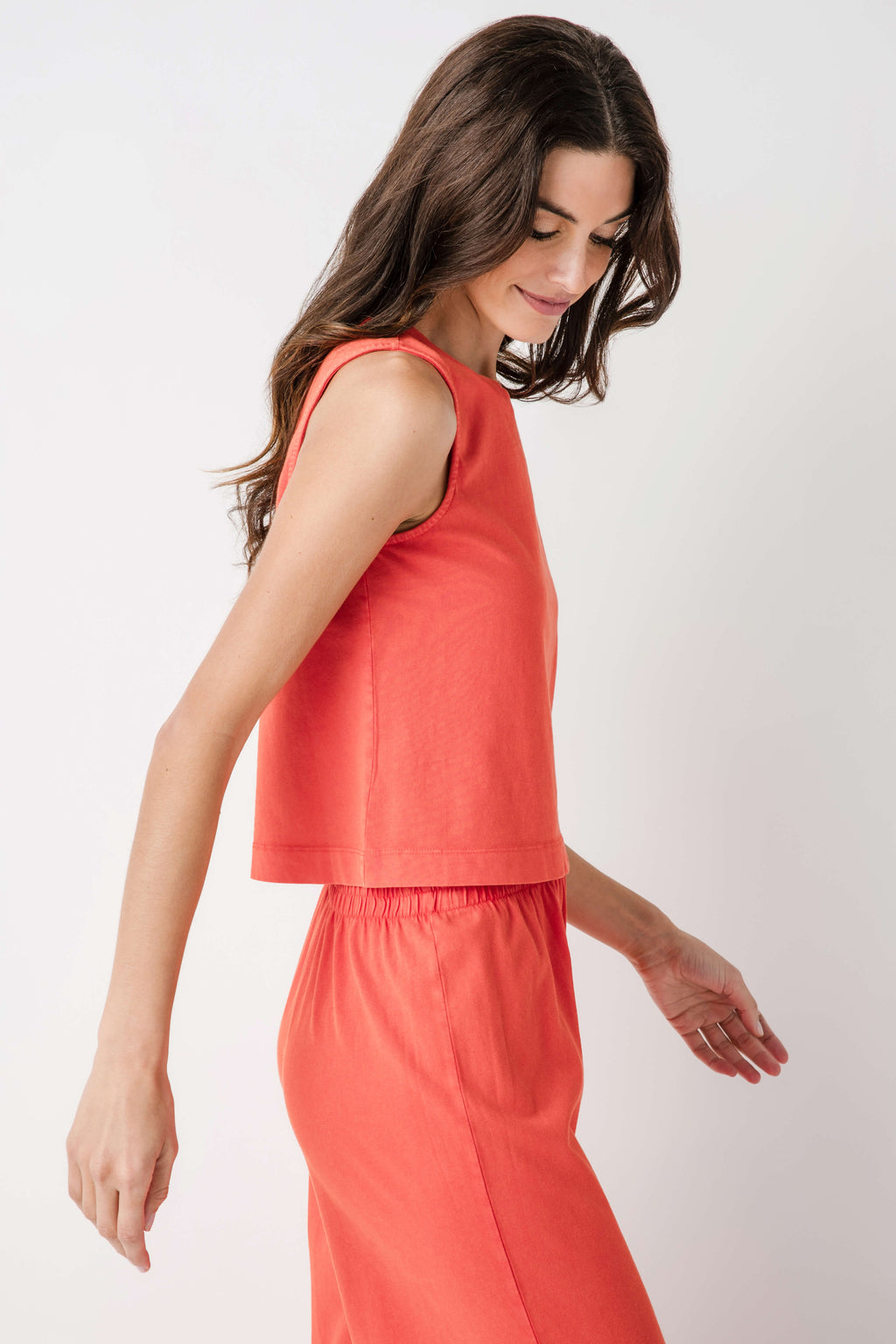 Coral sleeveless muscle tank with crew neck and relaxed tiered hem; paired pants.