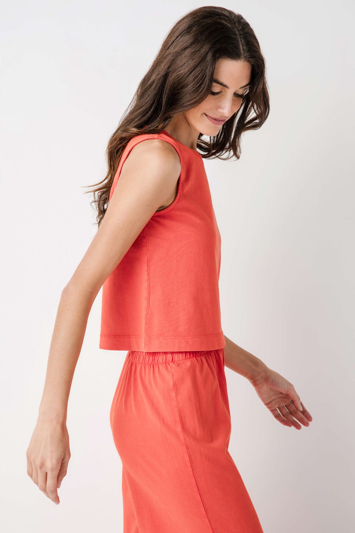 Coral sleeveless muscle tank with crew neck and relaxed tiered hem; paired pants.