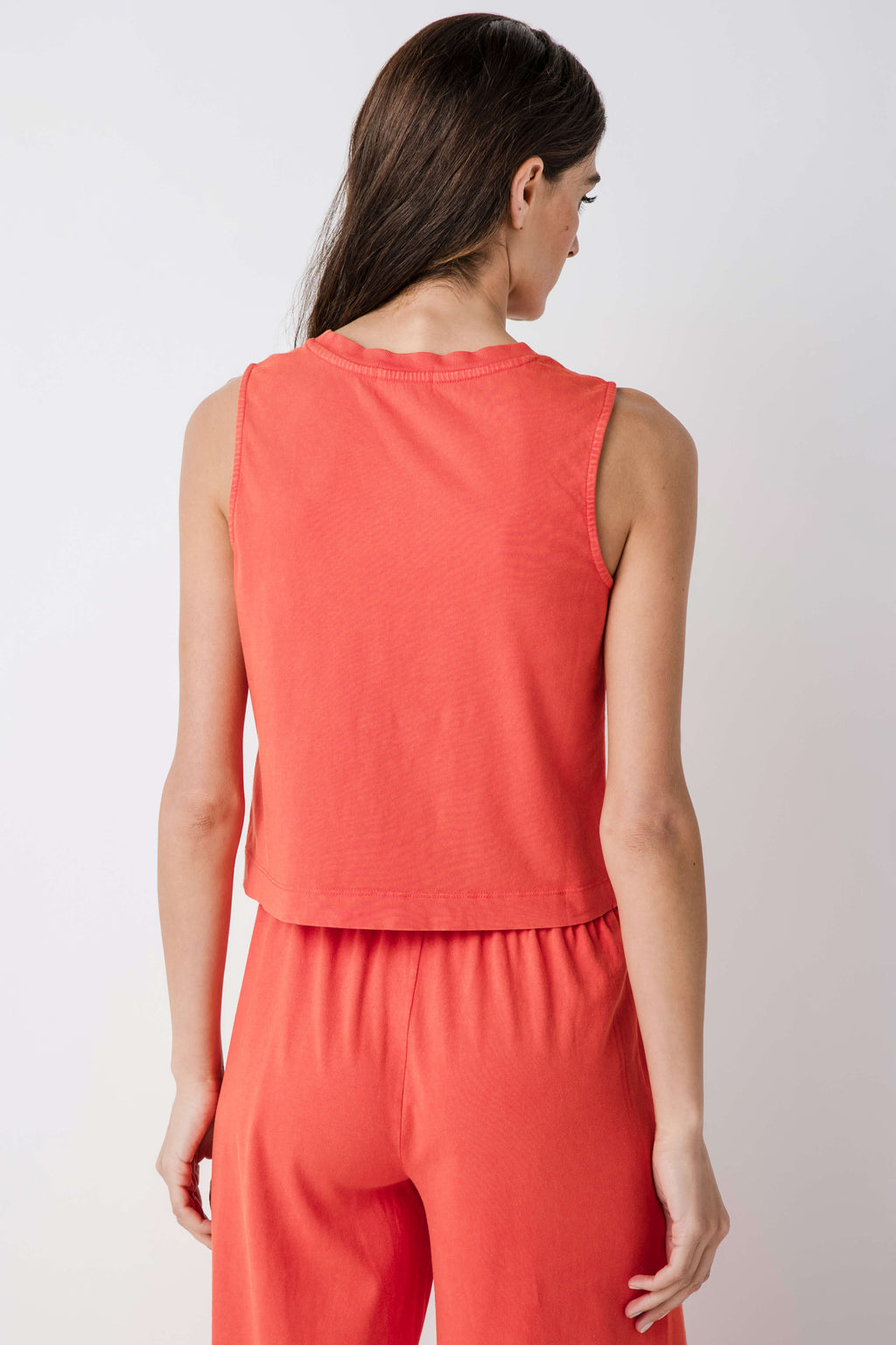 Back view of coral sleeveless jersey tank with crew neck and tiered, gathered hem.