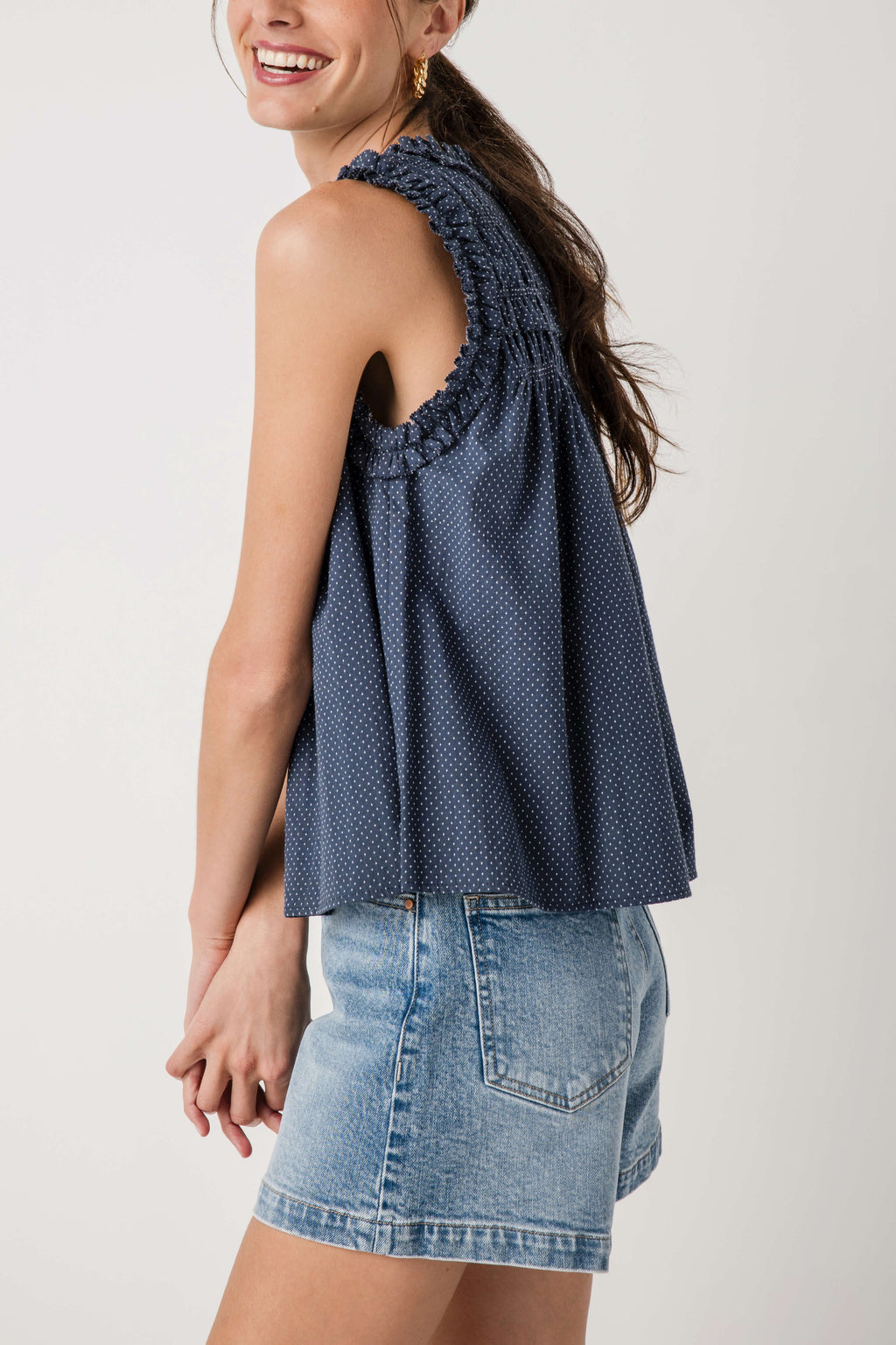 Navy sleeveless smocked birdseye top, side view with high ruffle neckline