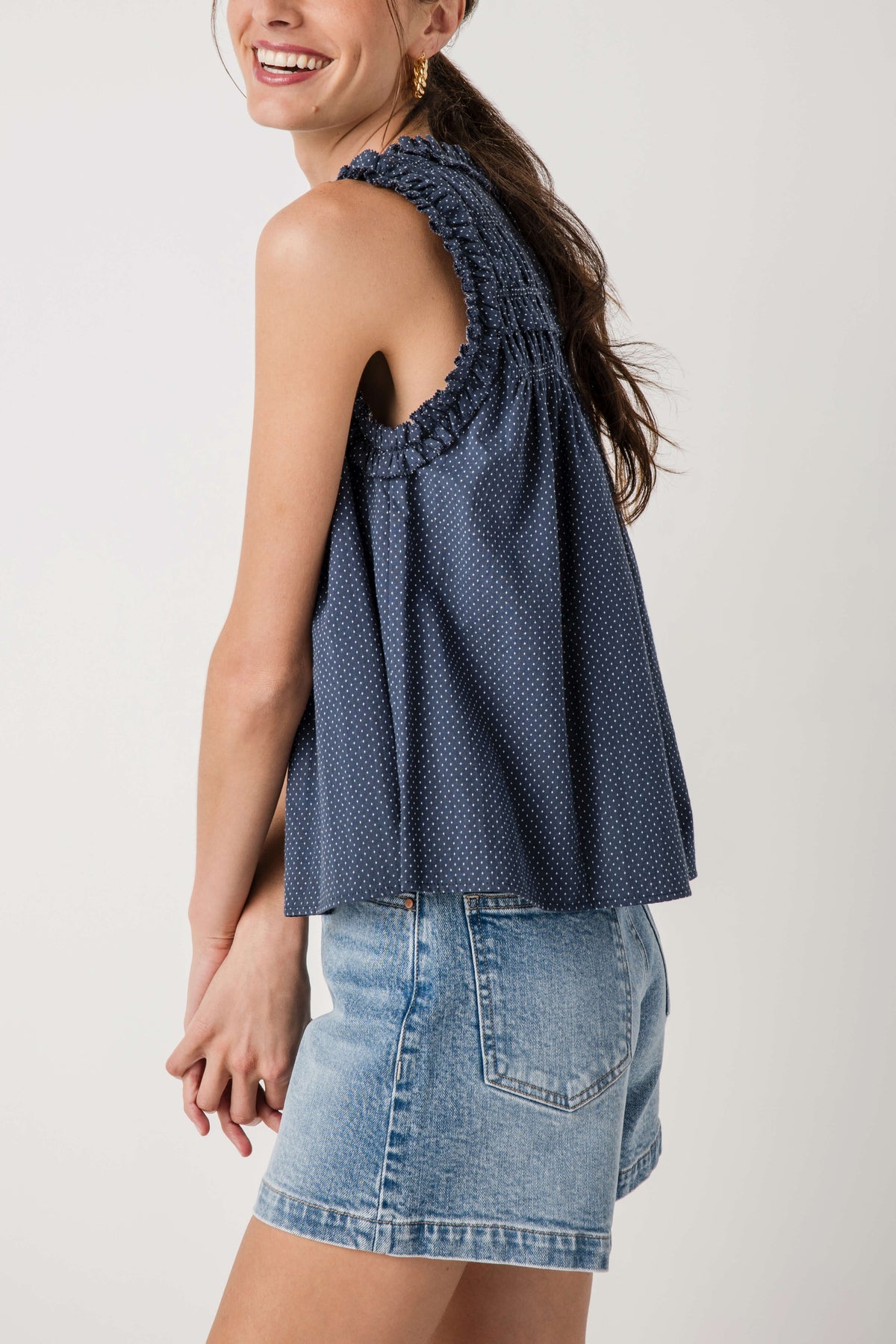 Navy sleeveless smocked birdseye top, side view with high ruffle neckline