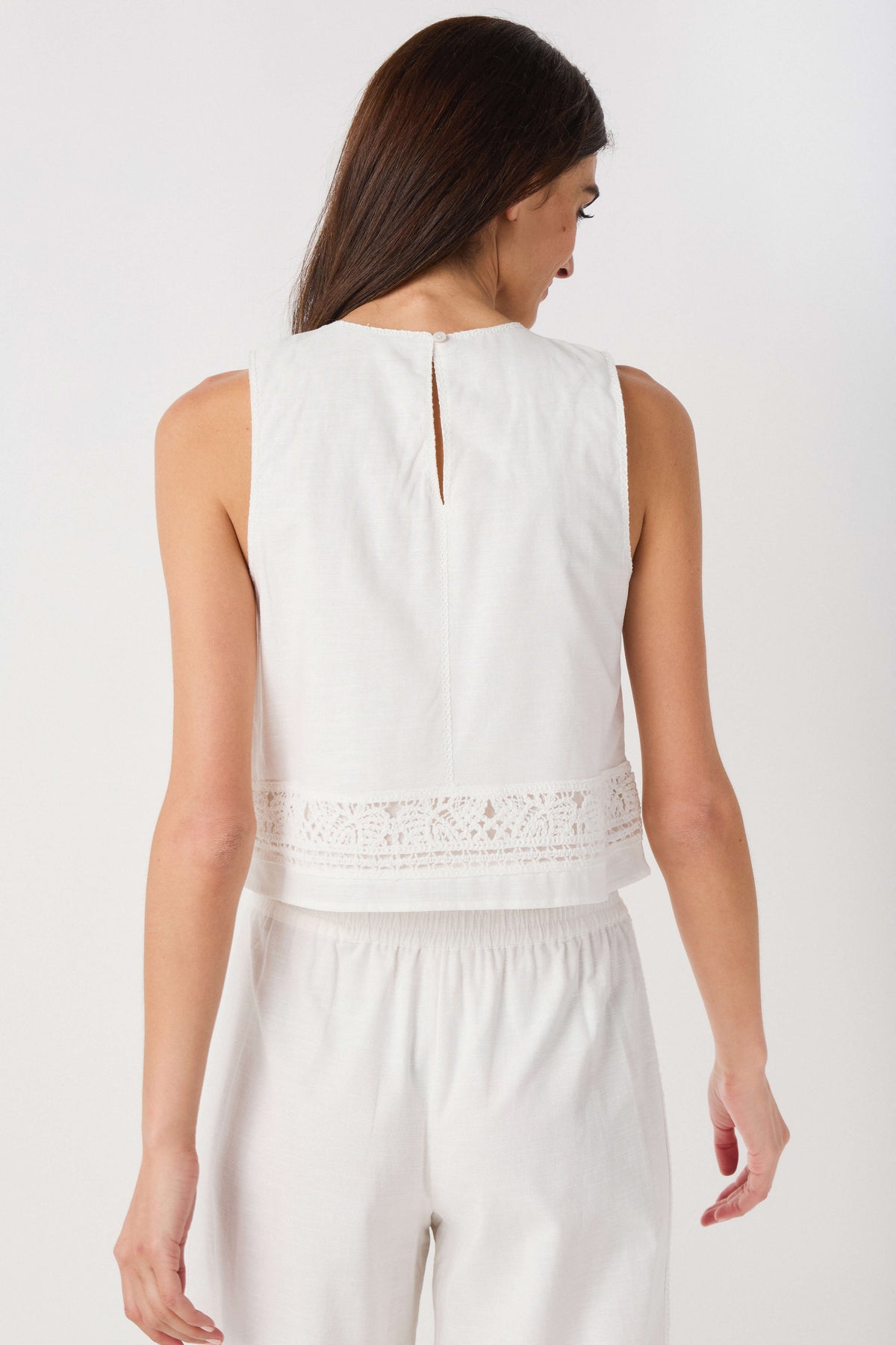 White sleeveless embroidered top, back view, with keyhole opening and lace-trim hem