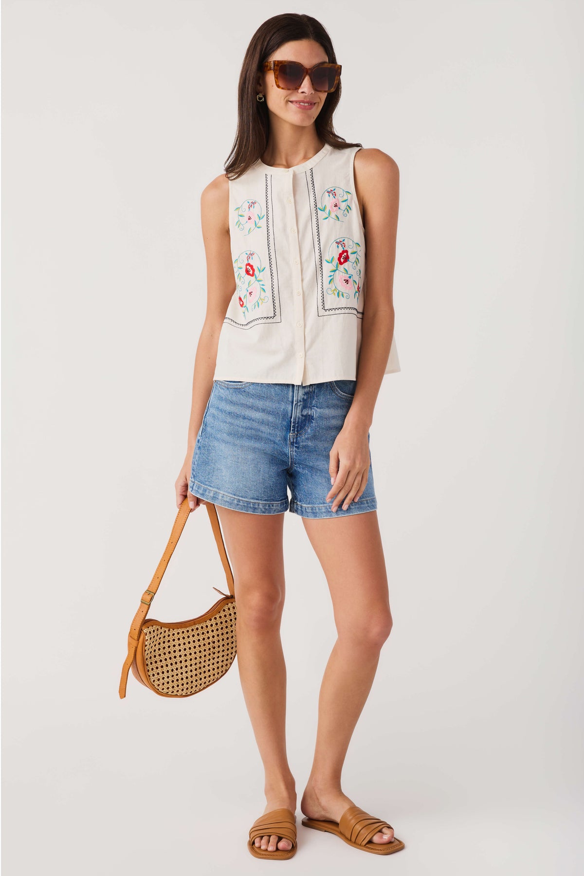 Tan rattan crossbody bag worn with perforated woven circle body and adjustable strap
