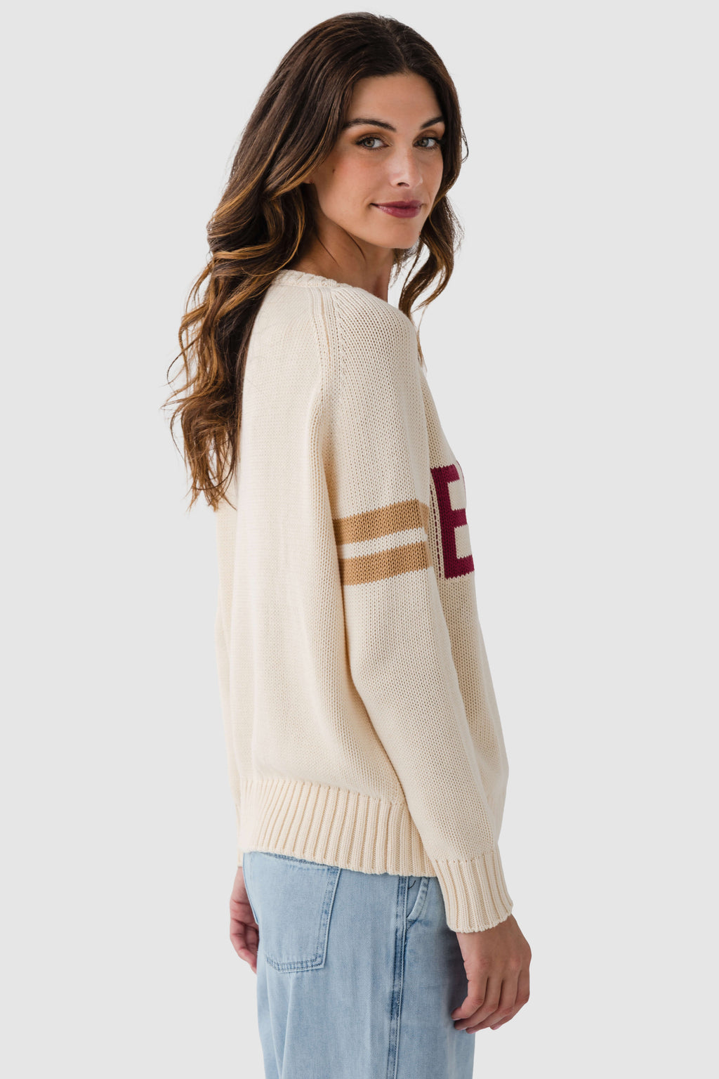 Cream knit sweater with maroon sleeve letter graphic and tan-and-navy stripe detail