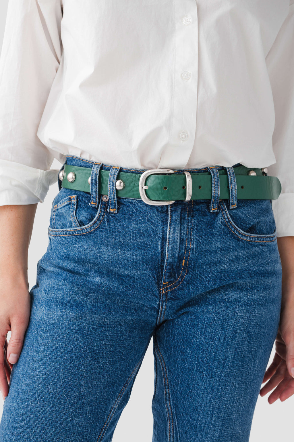 Emerald stud belt with square buckle and gold eyelets, worn on jeans