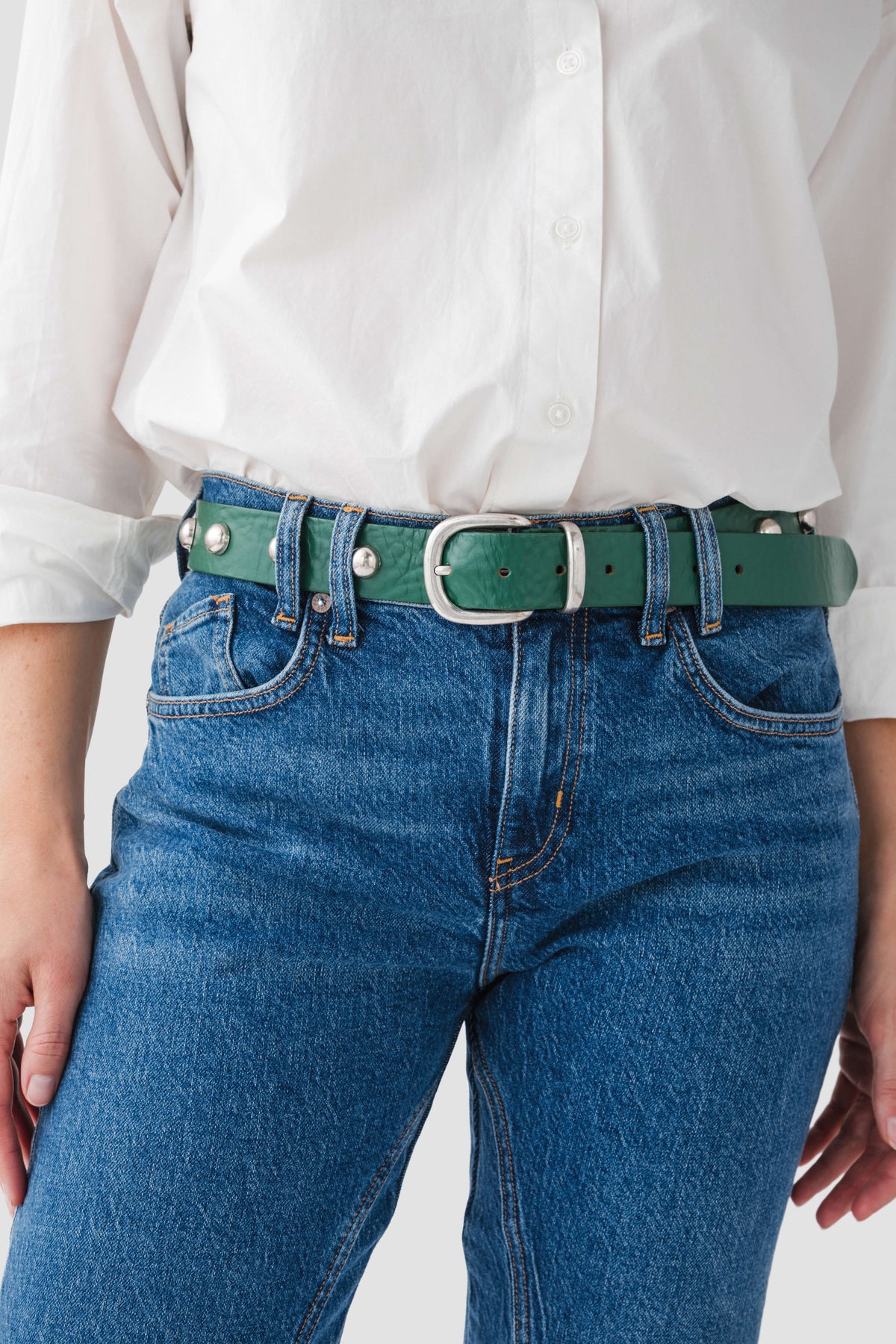 Emerald stud belt with square buckle and gold eyelets, worn on jeans
