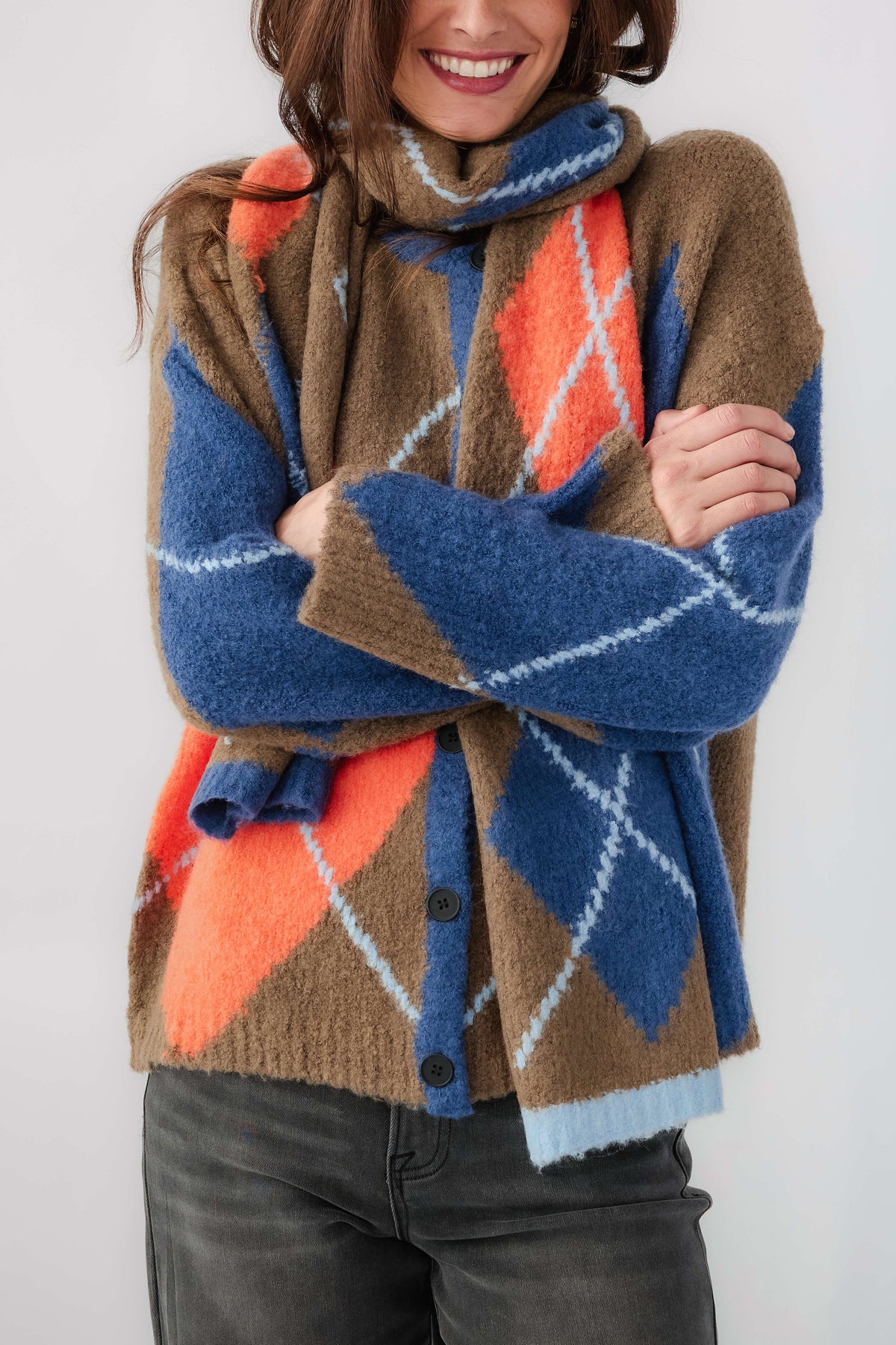 Kaki plaid scarf with blue and orange diamonds, worn with arms crossed
