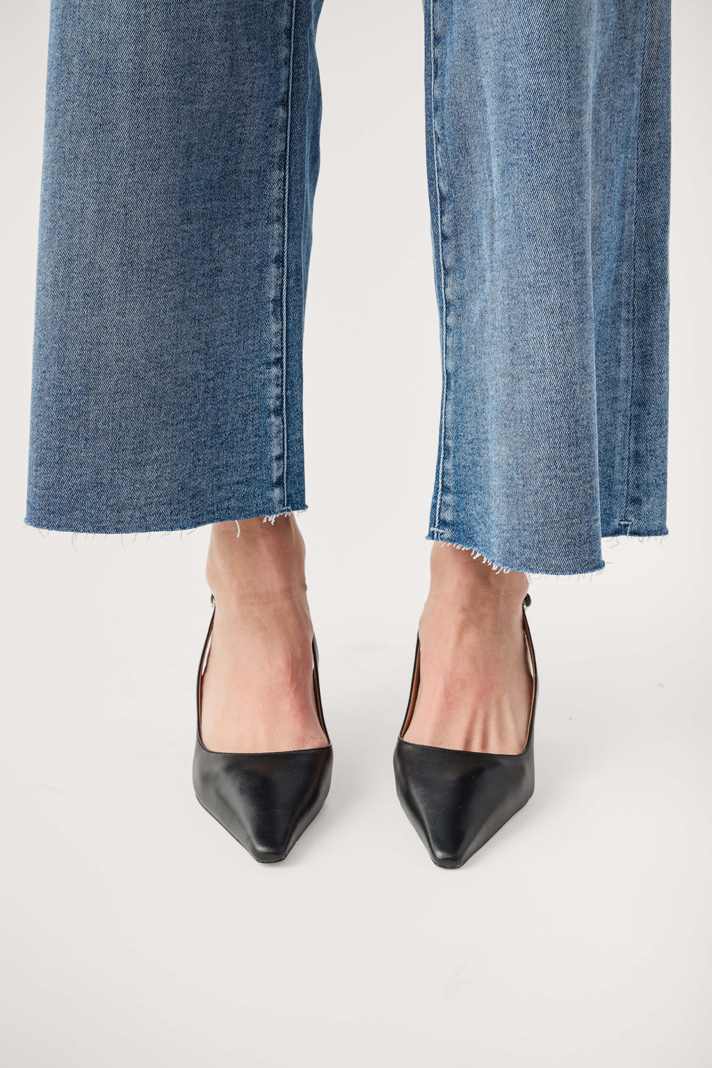 Black leather slingback pump with pointed toe and slim high heel, worn with jeans.