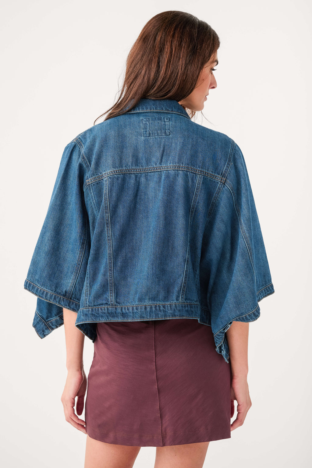 Back view of cape-sleeve denim jacket in medium blue wash with button detail