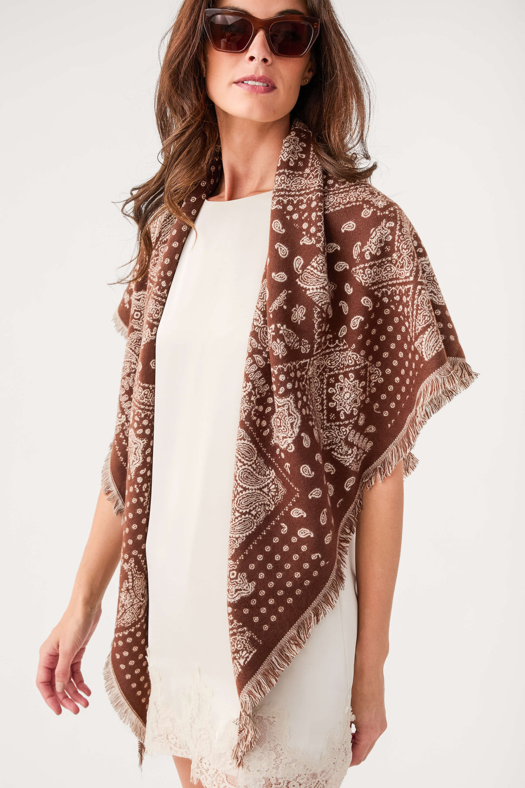 Brown bandana print scarf with repeating motifs and fringed ends worn over shoulder