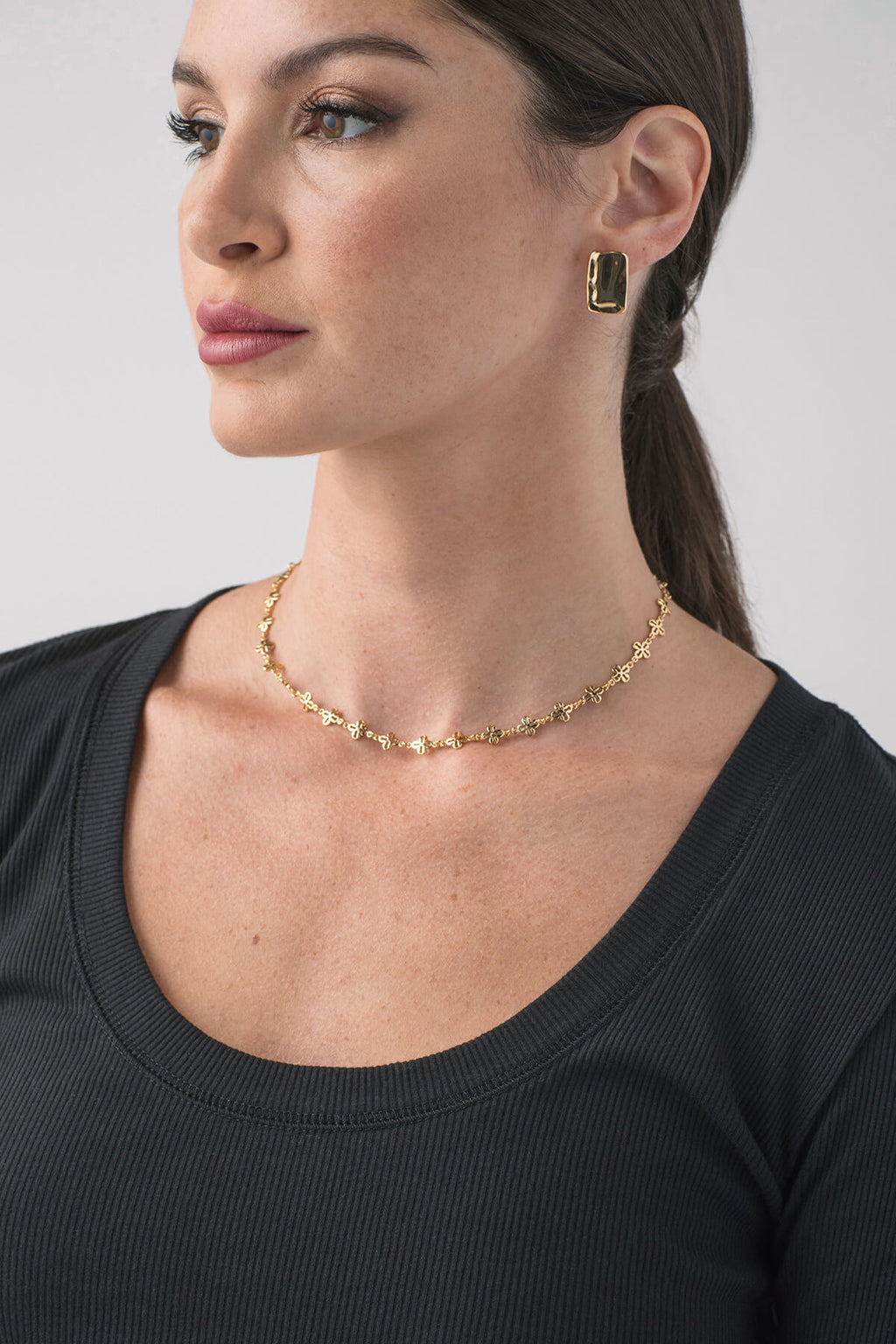 Gold criss-cross chain necklace with small charm links, worn at collarbone
