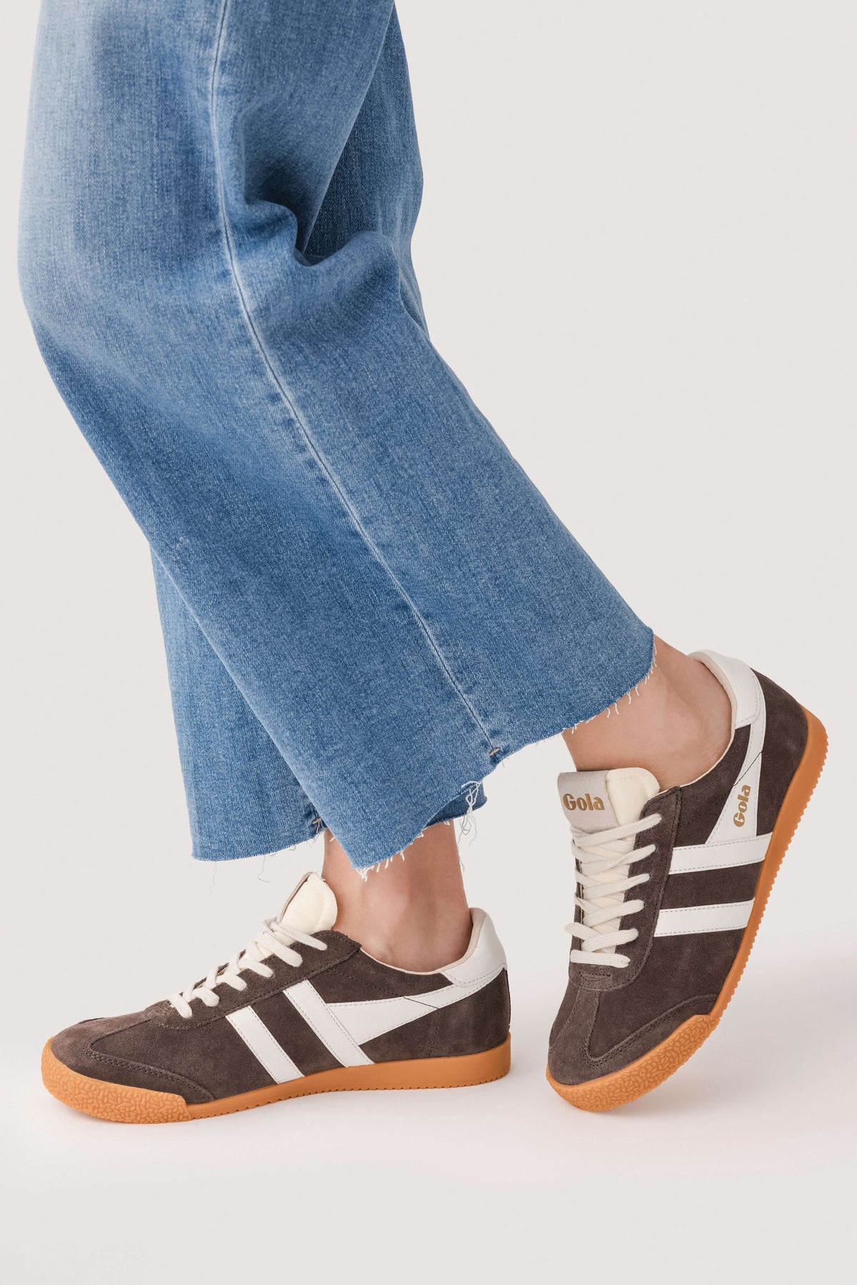 Brown low-top sneakers with white stripes, white laces, and gum sole.