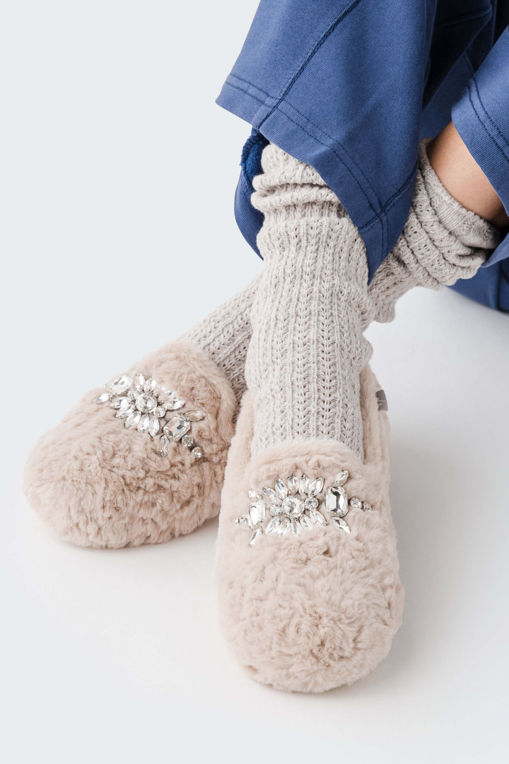 Light beige fuzzy slipper with ribbed knit cuff and silver floral jewel applique on the side.