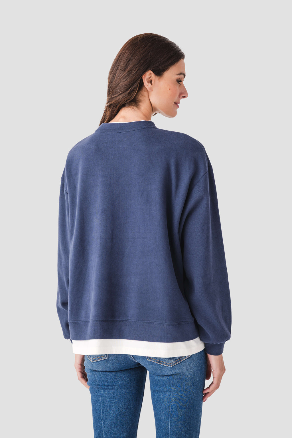 Back view of blue crewneck pullover with ribbed cuffs and hem, white trim at bottom