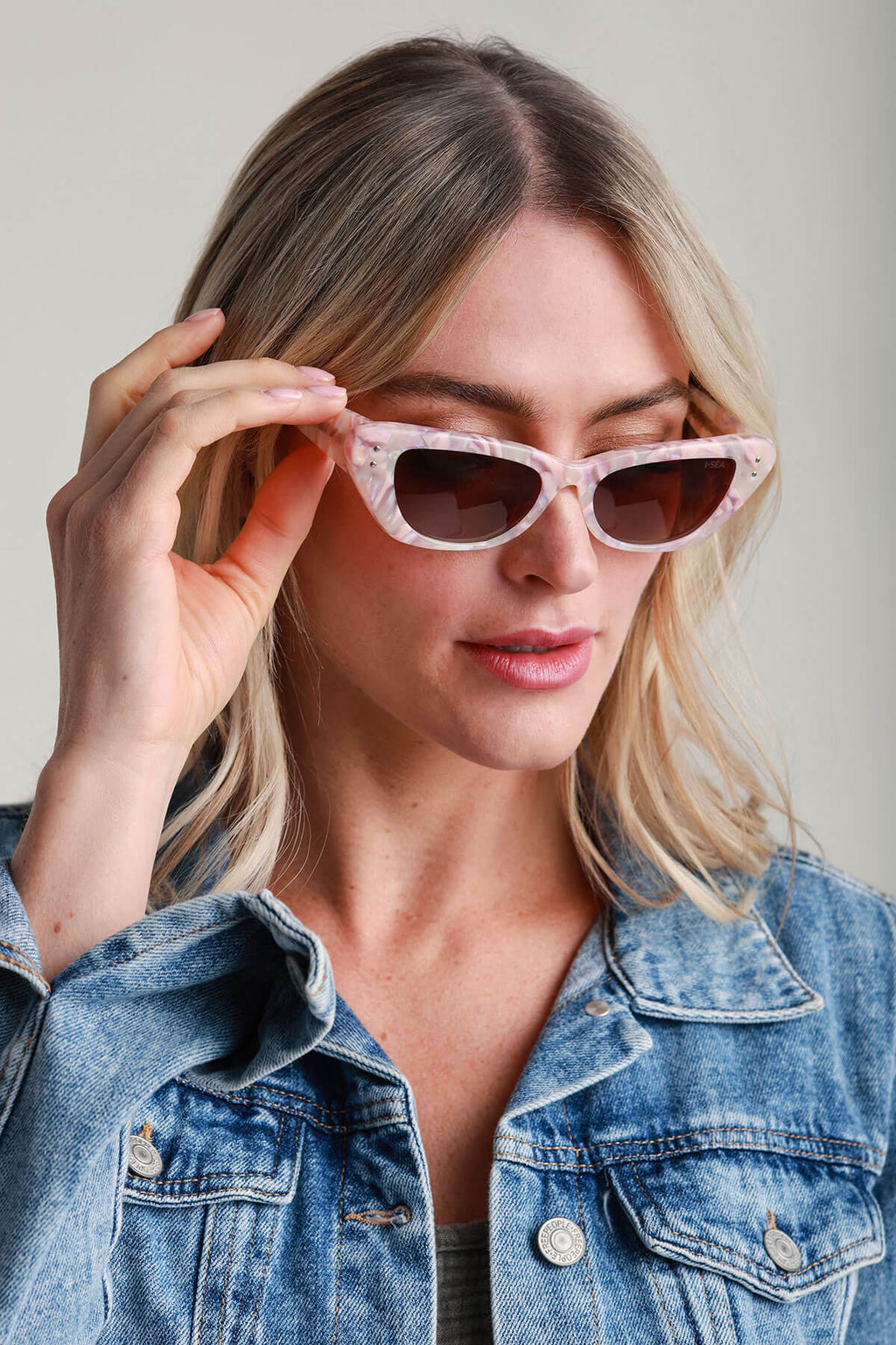 Cat-eye sunglasses with pink translucent frame and dark lenses, hand adjusting